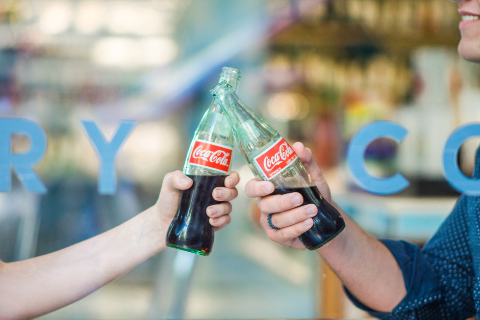 Two people cheersing coke bottles